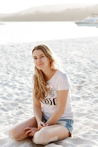 Carefree laughter a happy girl sits on a sandy beach and looks at the camera while enjoying her vacation. Stay in a resort hotel near the ocean.