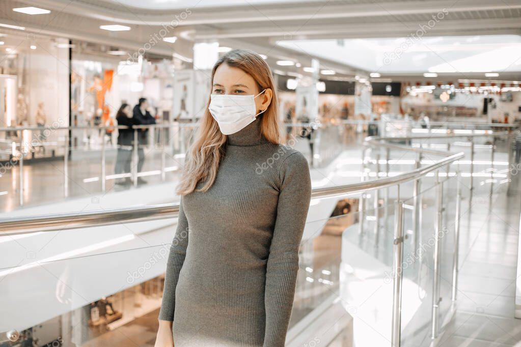 Young pretty woman wearing protective mask against coronavirus and looking away while standing in shopping mall. Portrait of a caucasian woman wearing face protection in prevention for coronavirus in Europe. Free space for text or advertising. 