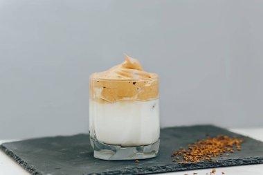 Gri arka planda sütlü, tüylü, yumuşak, Kore kremalı bir Dalgona kahvesi. Kore 'den moda ev yapımı içecek. Açık gri arka planda soğuk yaz içeceği. Seçici odaklanma. Çırpılmış dalgona kahve konsepti.