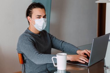 Evde koruyucu maskeli, COVID-19 virüslü sıkıcı bir bilgisayarda çalışan hasta bir ofis çalışanı. Coronavirus salgınının sosyal mesafesi evden kaynaklanıyor. Evde kal, sıkıcı düşük üretkenlik konsepti.