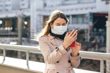 Koronavirüs pandemisi sırasında sokakta cep telefonuyla gezen bir kadın virüs hastalığından korunmak için yüz koruyucu maske takıyor. COVID-19 Salgını. 