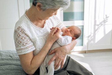Büyükannesi tatlı torununa hayran. Büyük büyükannem yeni doğmuş büyük torunuyla oynuyor. Bebek büyükannenin kollarında yatıyor.