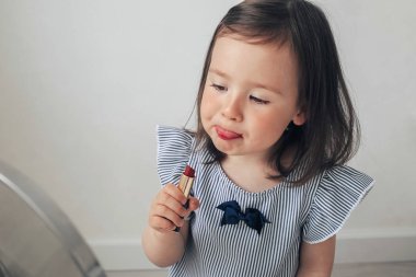 Güzel kız makyaj yapıyor. Küçük kız annesinin makyajıyla oynuyor. Komik makyaj bebeği. Modaya uygun bir kadın gözlerini ve dudaklarını boyar. Aynada mavi bluzlu bir kız.. 