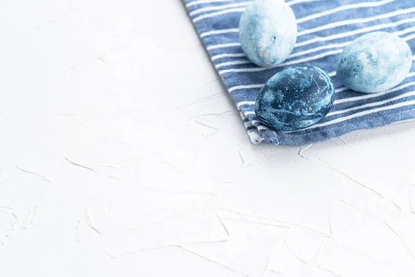 Ovos de Páscoa azuis numa toalha azul. Três ovos no canto da moldura em um fundo branco. Páscoa em azul — Fotografia de Stock