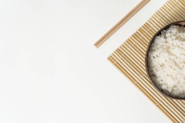 Beyaz arka planda hindistan cevizi kasesinde beyaz pirinç. Pirinç ve bambu çubuklu minimalist fotoğraf.