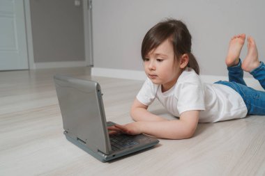 Happy girl communicates online with friends. The child won the computer game and rejoices. Child at home during a pandemic clipart