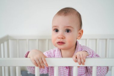 Pembe pijamalı küçük bir çocuk beşikte duruyor. Çocuk uyandı ve ailesinin onu beşiğinden çıkarmasını bekledi. Bebek ağlamaya başlar
