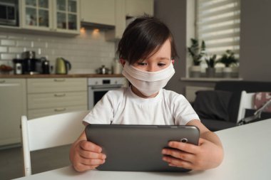 Çocuk salgın sırasında internetten öğreniyor. Maskeli bir anaokulu öğrencisi evde eğitim görüyor. Çocuklar için modern uzaklık eğitimi.