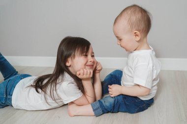 İki küçük kız kardeş sevimli oynuyorlar. Beyaz tişörtlü ve kot pantolonlu çocuklar. Küçük kız kardeş büyük olana bakıyor..