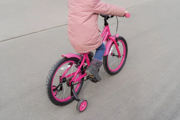 Un bambino va in bicicletta con una giacca rosa. Un bambino con le spalle al fotografo. Passeggiate primaverili vicino alla casa in bicicletta . — Foto Stock