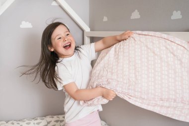 Neşeli kız yastık savaşı yapıyor. Çocuk yatağa dalıp yastıklarla savaşıyor.