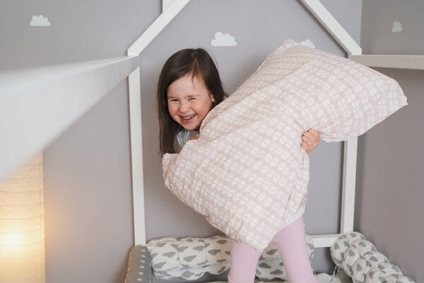 Cheerful girl playing pillow fights.The child indulges in the bed and fights pillows.