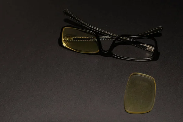 Óculos com uma borda preta quebrada jazem em uma superfície preta — Fotografia de Stock