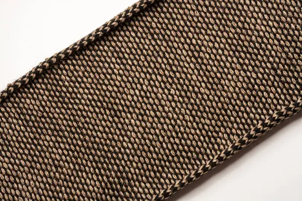 Фрагмент в'язаного шарфа коричнево-чорного кольору зі скрученими краями. Діагональне розташування на білому тлі — стокове фото