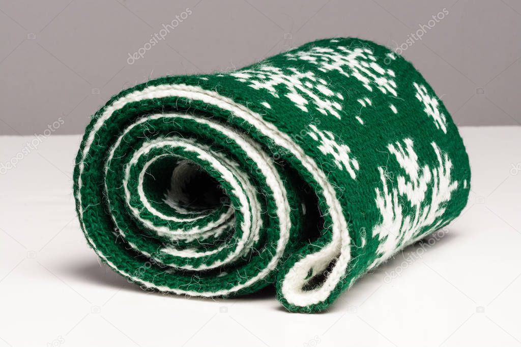 Twisted in a roll green scarf lies not a white surface on gray background