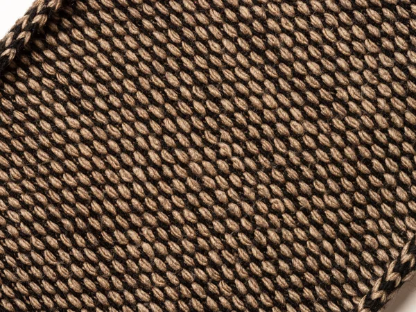 Фрагмент в'язаного шарфа коричнево-чорного кольору зі скрученими краями. Діагональне розташування на білому тлі. Крупним планом — стокове фото
