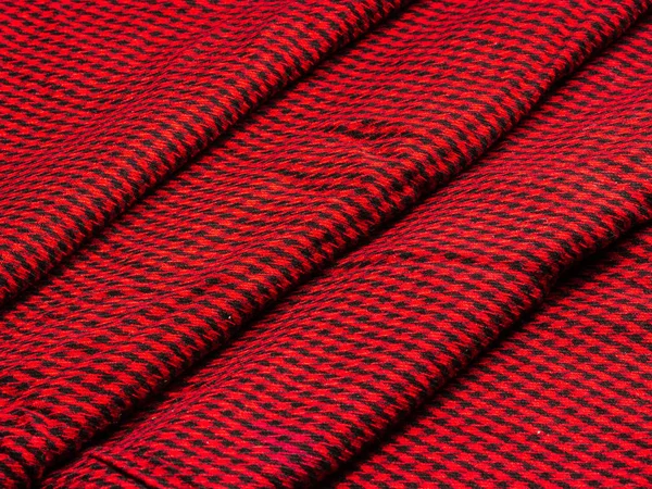 Paño de lana en una pequeña jaula negra sobre un fondo rojo apilado con una cascada de capas — Foto de Stock
