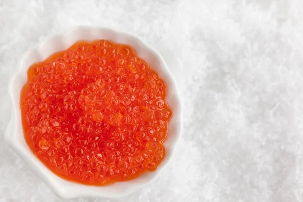 Delicioso caviar vermelho em tigela no fundo de neve branca — Fotografia de Stock