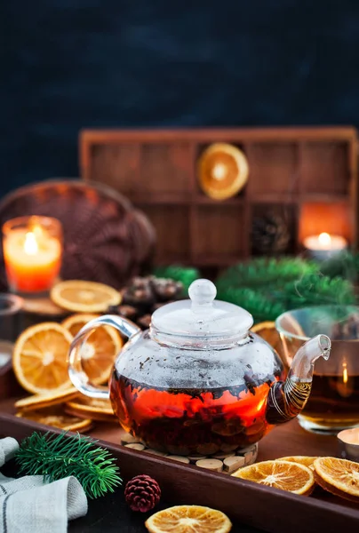 Glass teapot of hot black tea on cozy background with dried oran — Stock Photo, Image