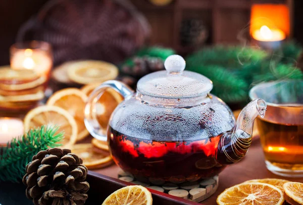 Glass teapot of hot black tea on cozy background with dried oran — Stock Photo, Image