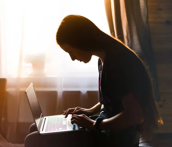 Evde eğitim, uzaktan eğitim, online eğitim, evde kalmak, karantina, teknoloji, modern yaşam tarzı. Evde pencerenin önünde dizüstü bilgisayar kullanan genç bir kız..