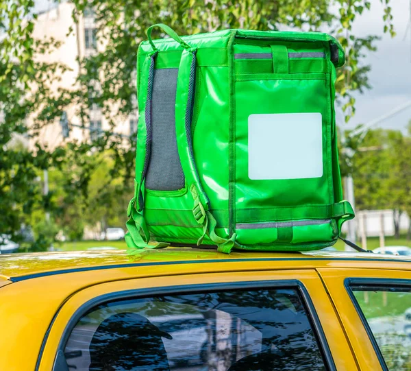 Closeup of green food delivery box, backpack standing on the top of yellow car. Mockup for food delivery service. Copy space
