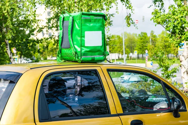 Green food delivery backpack standing on the top of yellow car. Mockup box for food delivery service. Copy space