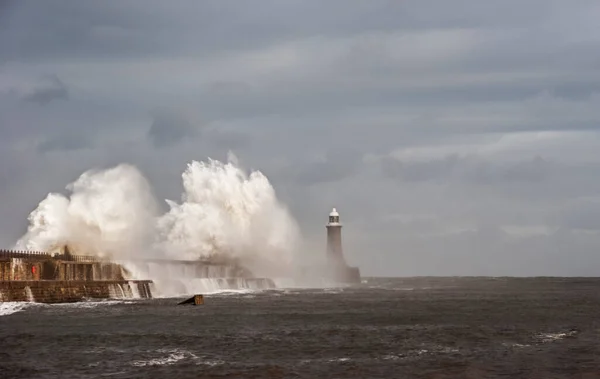 A wave crashes over Tynemouth pier and lighthouse