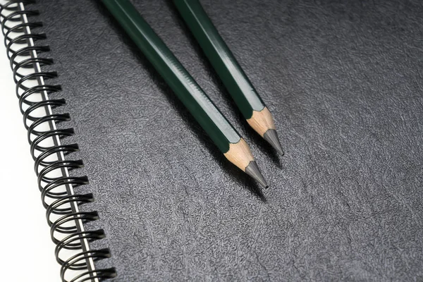 Two green pencils laying on a black ring binder — Stock Photo, Image