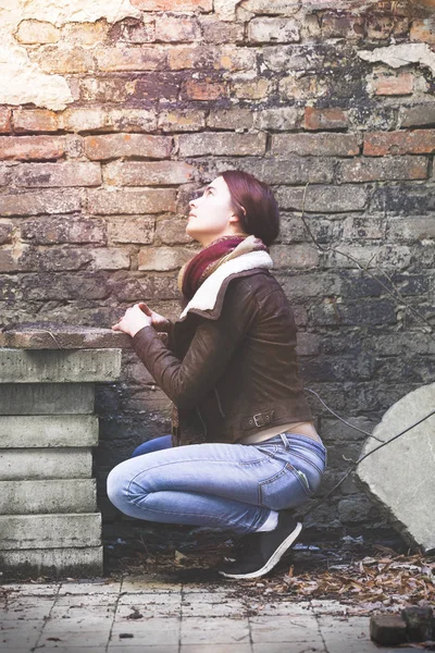 Mujer joven con chaqueta de cuero rezando frente a una vieja pared — Foto de Stock