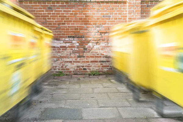 Pohybující se žlutá popelnici před červenou cihlovou zeď — Stock fotografie