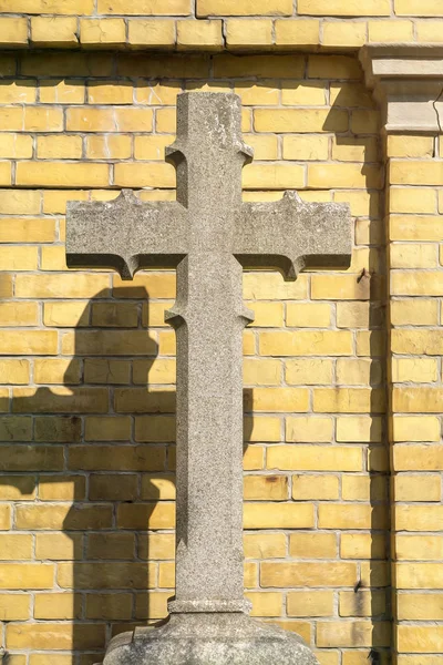 Croce di pietra davanti a un muro di mattoni gialli — Foto Stock