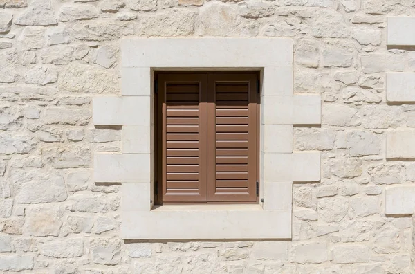 Окно с коричневыми ставнями и природной каменной стеной — стоковое фото