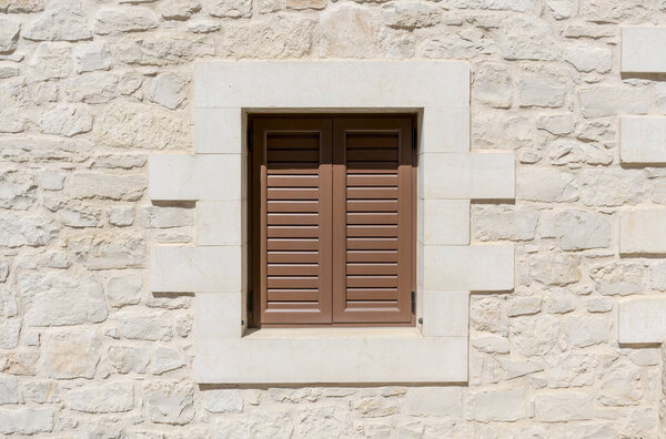 window with brown shutter and a natural stone wall