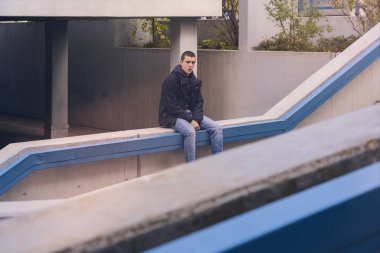 Beton duvarda oturan sıradan bir gencin portresi.