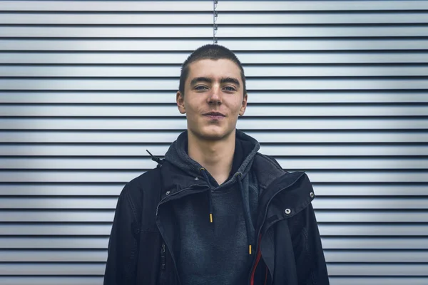 Portrait of a smiling young man in front of a silver roller shutter — Stock Photo, Image