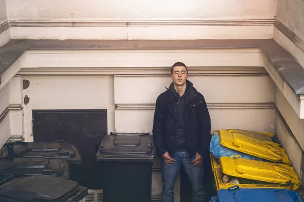 Портрет молодого человека с закрытыми глазами, стоящего между мусорными баками — стоковое фото