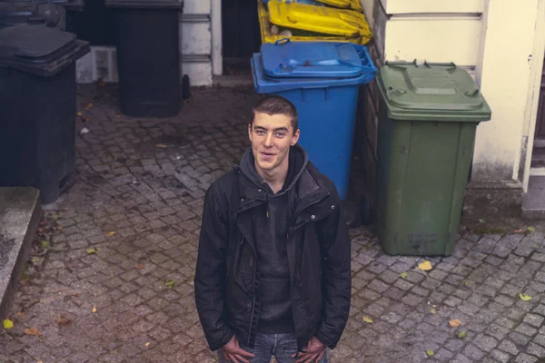 Retrato de um jovem casual em pé na frente de latas de lixo — Fotografia de Stock