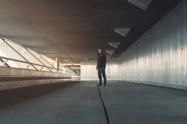 Siyah elbiseli genç adam metalle kaplı bir koridorda duruyor.