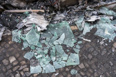 Yanmış bir arabanın önünde kırık camlar var..