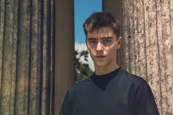 Portrait of a young man standing between ancient columns — Stock Photo, Image