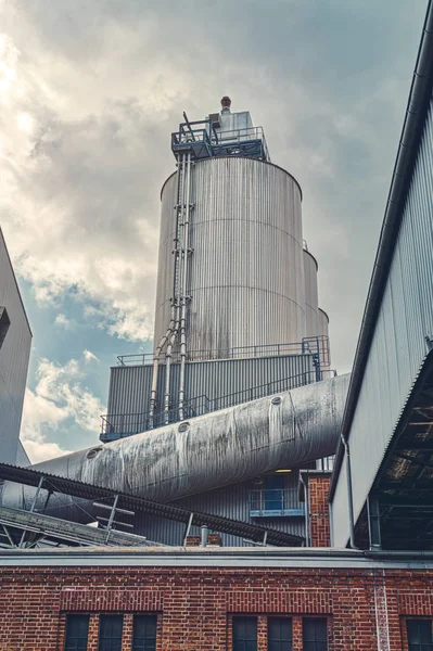 Trois silos et un grand tuyau d'une usine au ciel dramatique — Photo