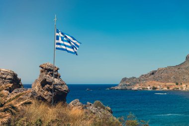 Kayalık bir körfezde rüzgârda Yunan bayrağı