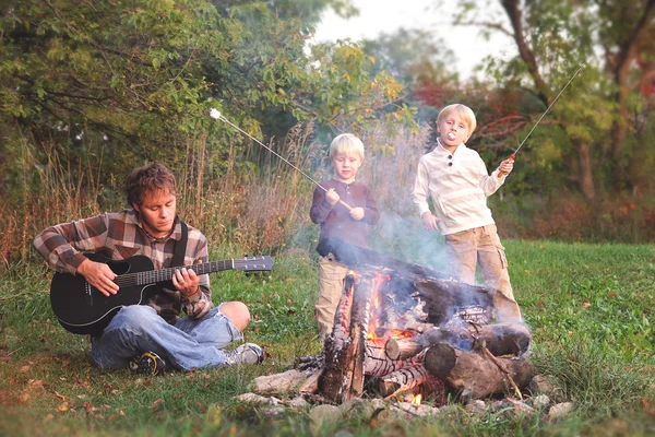 Pai e filhos assando marshmallows e tocando guitarra pelo acampamento — Fotografia de Stock