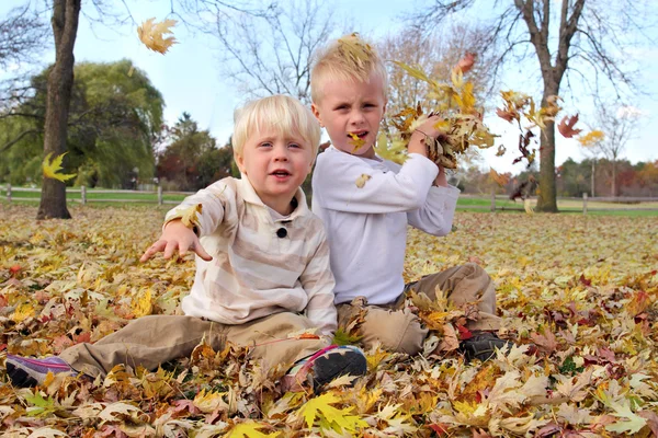 Bambini felici lanciando foglie di acero caduta a macchina fotografica — Foto Stock