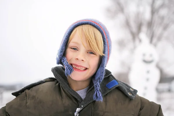 Felice bambino fuori a giocare nella neve dopo la costruzione pupazzo di neve — Foto Stock