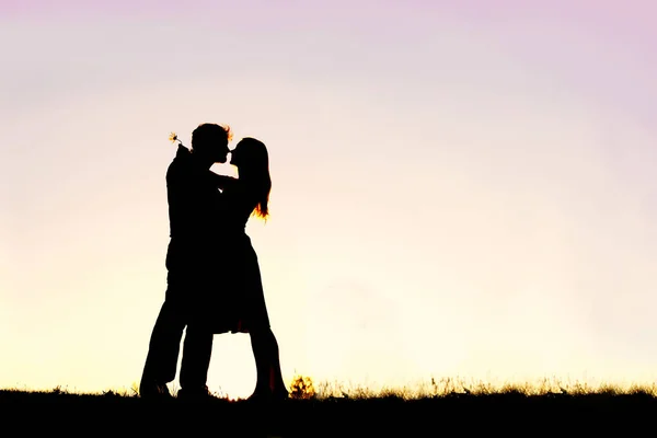 Silueta milující, mladý pár objímání při západu slunce mimo — Stock fotografie