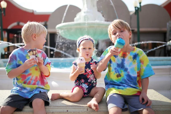 三个年轻孩子吃冰激凌喷泉旁在夏季的一天 — 图库照片