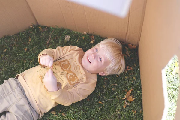 Jonge kind leggen in gras terwijl Playing in kartonnen doos Fort — Stockfoto