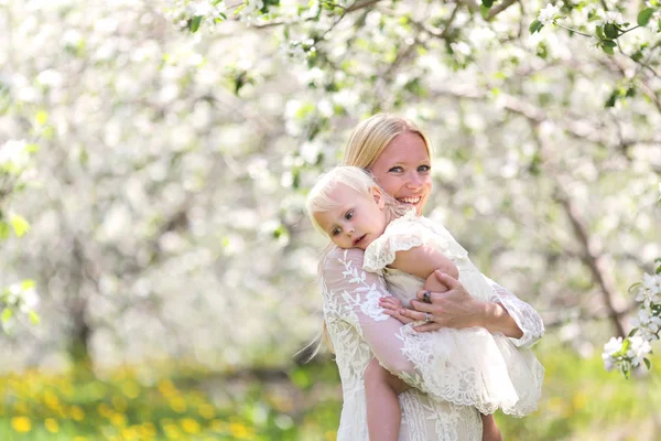 Madre feliz abrazando a la hija en el huerto de manzanas florecientes — Foto de Stock